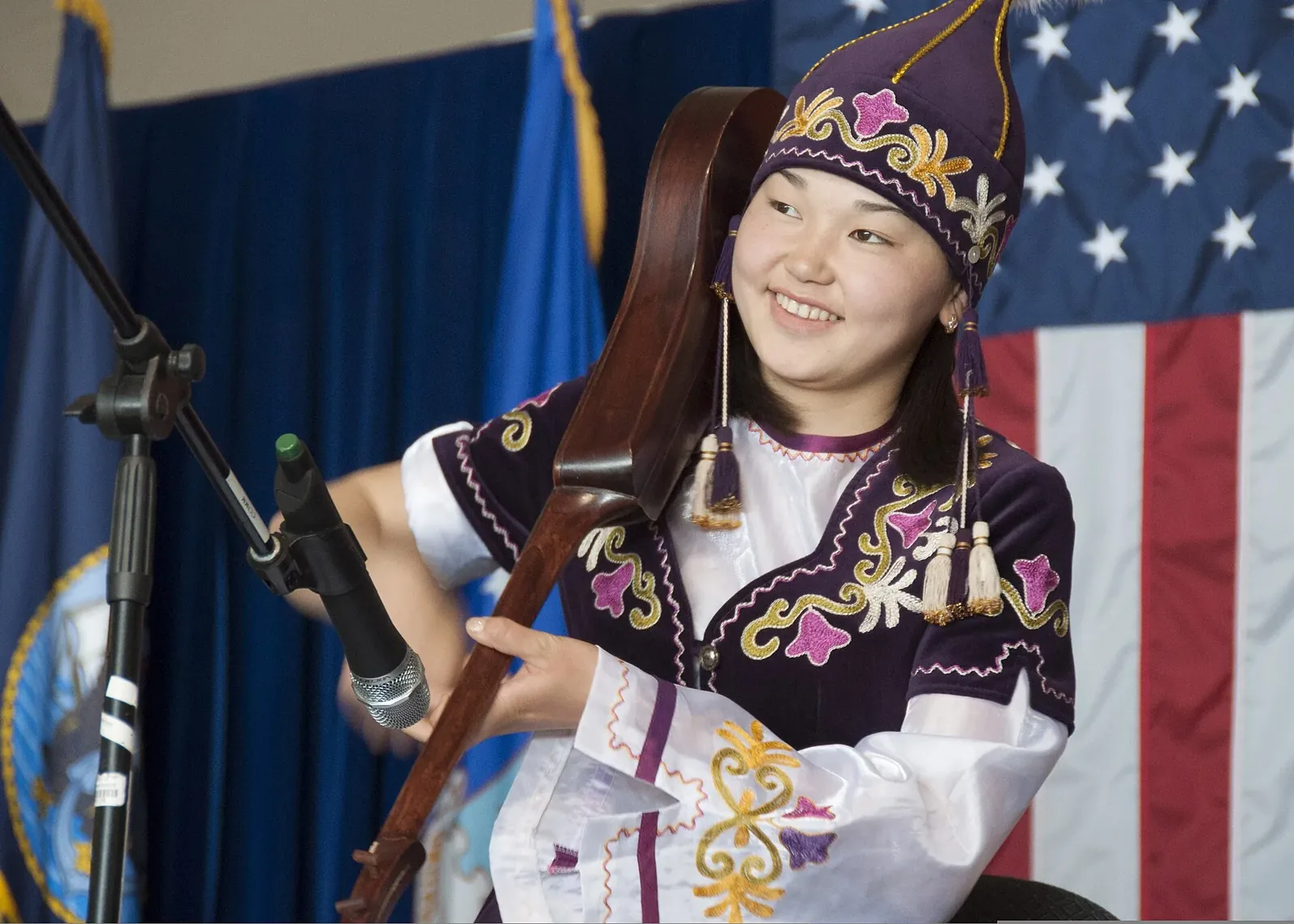 A Mukash Abdraev National School of Music student, dressed in a traditional Kyrgyz outfit, plays the komuz during a concert, April 4, 2013, at the Transit Center at Manas, Kyrgyzstan. The komuz, a fretless string instrum. Фото: TSgt Rachel Martinez, Public domain, Викисклад